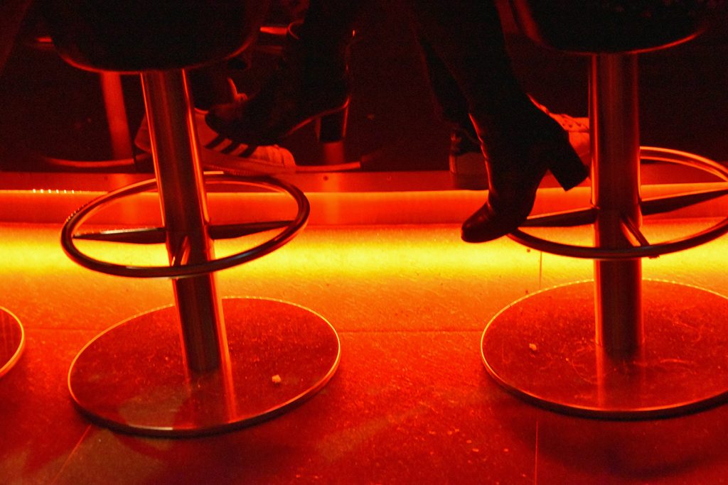 shot of the bottom of two barstools with patrons' feet in a colorfully lit bar